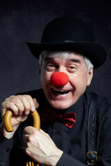 Portrait of laughing  clown against a dark background leaning on the handle of an umbrella.