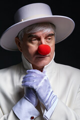 Close-up portrait of sad clown. An elderly man in a white coat and hat.