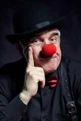 Dramatic portrait of a sad clown against a dark background.  Hand near face.