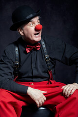 Portrait of a clown on dark background  with red clown nose and bowler hat on head.