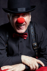 Portrait of a clown with a hat pulled down over his eyes sticks out his tongue.
