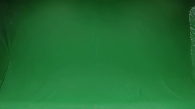 A studio space featuring a green backdrop and lighting fixtures. A clear sheet hangs down