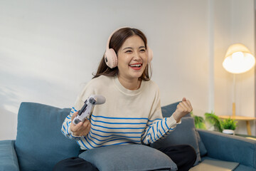 A young woman wearing headphones is sitting on a sofa while holding a game controller, showing joy, excitement, and focus as she plays a video game indoors.