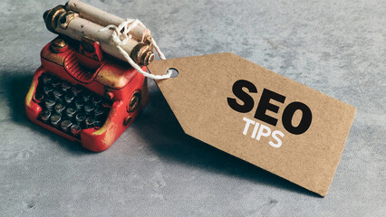 SEO Tips Message on Craft Tag Next to Miniature Vintage Red Typewriter on Gray Background