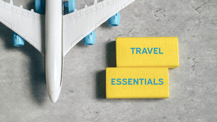 Travel Essentials Text on Yellow Wooden Blocks Next to Model Airplane Wing