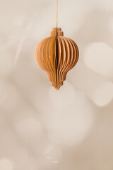 Craft paper Christmas ornament, beige colored New year flashlight hanging on gold string, blurred monochrome background. Christmas ball, winter holiday xmas decor, side view, honeycomb scandi style.