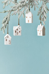 Set Small houses Christmas bauble hanging on snow green branch on blue background, New Year decor as symbol of estate, mortgage, insurance, new home,  and cozy holiday, minimal winter festive photo.