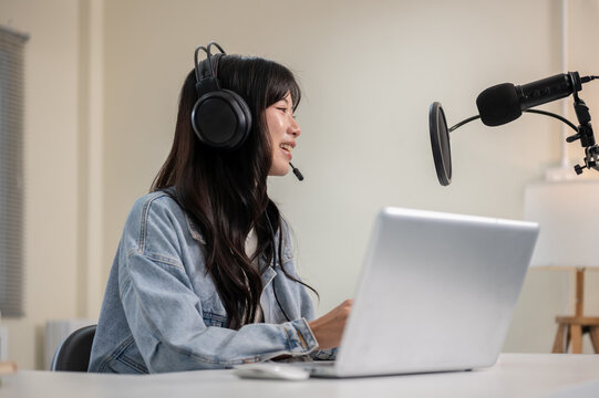 Asian woman talking hosting a radio or podcast through laptop with headset and mic at home or studio