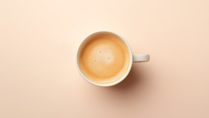 Overhead view of a white coffee mug filled with light brown coffee on a pale peach background