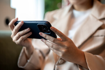Close up of woman holding smartphone horizontally while sitting on green sofa or armchair in a cafe.