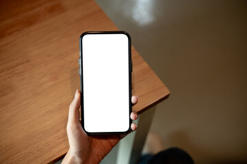 Close up of woman holding blank screen smartphone with one hand on wooden table in a cafe or library