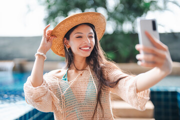 Young Hispanic Gen Z Woman Using Smartphone to Update Social Media by Resort Pool During Summer Vacation.