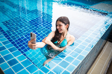 Young Hispanic Gen Z Woman Using Smartphone to Update Social Media by Resort Pool During Summer Vacation.