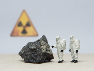 Mini toy of action figure at table with blur background. Miniature photography concept design. Minifigure of worker character wearing hazmat suit with uranium stone and radioactive symbol. © awstoys