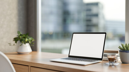 White screen laptop and coffee aside potted plant on wooden table with cityscape outside glass wall.