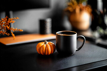 Minimal black coffee mug with small pumpkin on modern office desk in autumn atmosphere