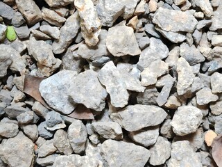 Gravel textured background. Close-up of gravel and dried leaves, rough texture, varied rock sizes and colors, potential use for landscaping purposes.