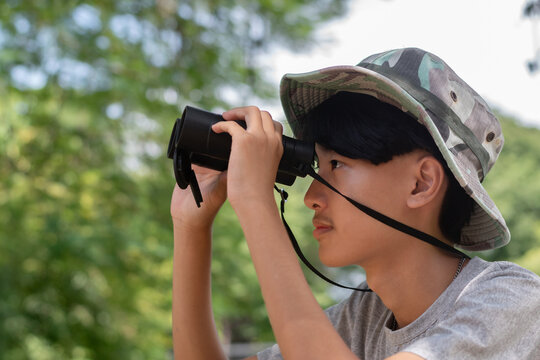A young explorer in a camo hat holds his binoculars, taking a moment to pose while observing nature outdoors.