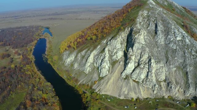 An aerial shot of the Shihan Yuraktau, a solitary mountain and a remnant of an ancient coral reef, located in the South Ural region of Russia. The footage captures the mountain's rocky slopes and the 