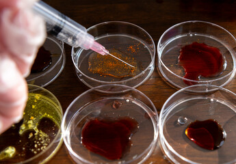 A close up of a laboratory researcher using a syringe to inject samples into petri dishes arranged in rows on a table top.