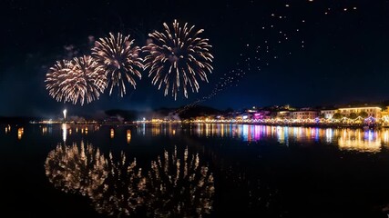 Colorful fireworks illuminate the night sky over a coastal town with reflections