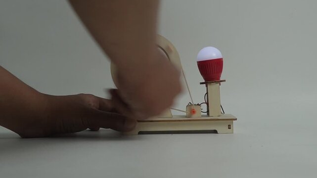 A hand is about to spin a small, handmade wooden generator with a flywheel and light bulb. This image is perfect for concepts of renewable energy, physics, science projects, and simple engineering.