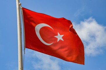 The Turkish flag flutters in the wind against a blue sky
