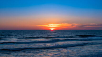 Obraz premium Blue Orange Sunset Over Dark Ocean Waves with Clear Sky