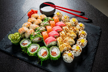 A vibrant array of sushi rolls is elegantly arranged on a dark slate platter, ready to share