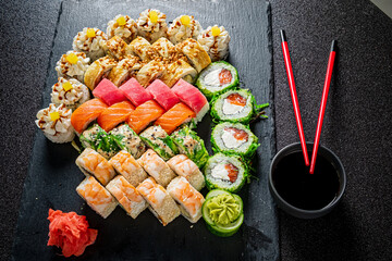A colorful display of sushi rolls and fresh fish served on a dark slate board with chopsticks