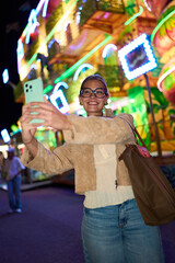 Young woman taking selfie at amusement park night