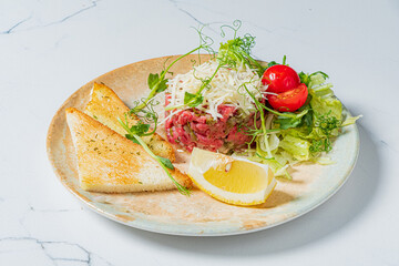 A vibrant plate features tartare, crispy toast, fresh greens, and a lemon wedge, ready to enjoy