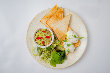 Enjoy a delicious plate featuring poached eggs, creamy guacamole, crisp salad, and toasted bread