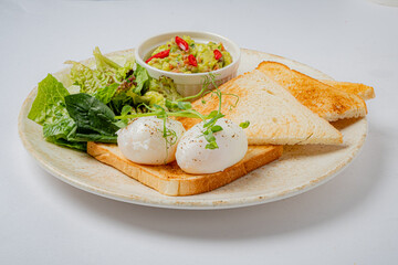 A vibrant brunch spread includes poached eggs, toasted bread, salad, and creamy guacamole