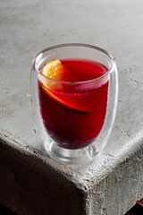 A vibrant red drink garnished with orange sits on a rustic table, inviting and refreshing