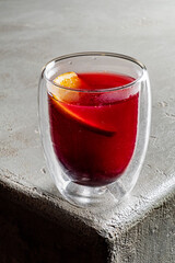 A vibrant berry beverage sits in a clear glass with an orange slice, inviting and enticing