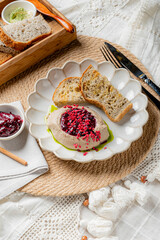 A creamy dish adorned with berry jam sits alongside toasted bread on a rustic table