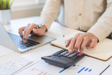 Account finance, asian young business man hand using calculator, laptop computer for calculate budget, cost and income of company from paperwork, plan spend money expenses, working on desk at home.