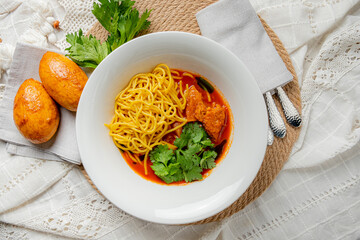 A bowl features golden noodles, tender chicken, and vibrant herbs on a textured surface