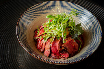 Sliced beef on vibrant greens creates a colorful, textured dish in a stylish bowl