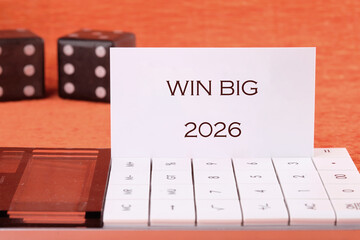 Two dice sit near a calculator, on which a card displays the text WIN BIG and 2026. This...