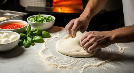 Fototapeta premium Hands kneading fresh pizza dough with basil, mozzarella, and tomato sauce on a marble counter, a wood-fired oven in background.