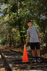 Young Boy Standing on Railway Tracks Holding an Orange Traffic Cone During a Sunny Afternoon in a Forested Area