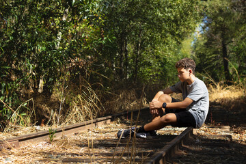 Young Boy Sitting on Abandoned Train Tracks Surrounded by Nature on a Sunny Day