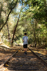 Young Person Walks Along Unused Railway Tracks in a Forested Area on a Sunny Day in Autumn