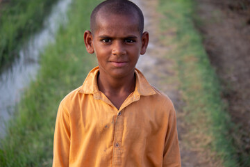 rural boy smiling near irrigation canal in village field, simple countryside portrait