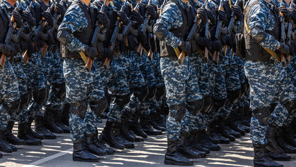 Many adult men marching in formation with assault rifles outdoors