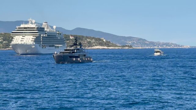 4k video footage from entrance of Port Hercules in Monaco with expensive luxury yacht entering the Port, a cruise ship anchored in the bay and mountain landscape and Cap Martin, France in background