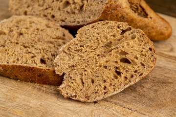 a sliced soft loaf of rye flour bread lies on the table on a cutting board, a small elongated loaf of freshly baked rye bread on an old cutting board while slicing bread