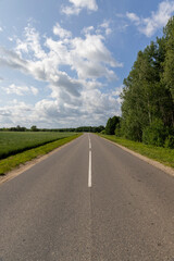 a paved road in rural areas in the summer with cloudy weather and a sky with lots of clouds, a narrow country road covered with asphalt